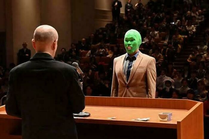 Man with green mask standing in courtroom facing a bald man at podium, highlighting fascinating photos and stories.
