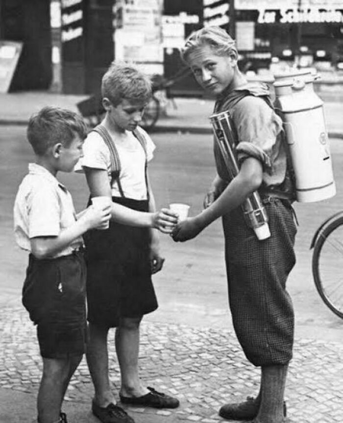 Three boys on a street, one with a milk container, sharing drinks in a fascinating photo capturing a different world view.
