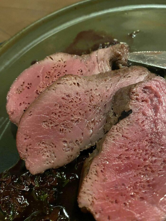 Close-up of cooked meat slices with irregular holes, creating a trypophobia nightmare fuel effect on the surface.