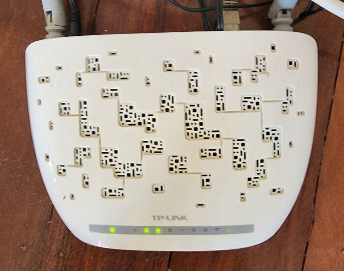 White TP-Link router with unusual small hole patterns resembling trypophobia-triggering clusters on a wooden surface