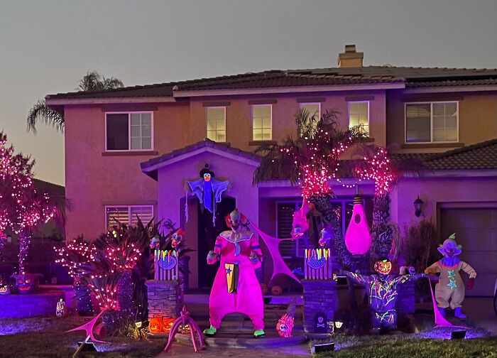 Outdoor Halloween decorations featuring colorful clown figures and purple lights illuminating a suburban home at dusk.