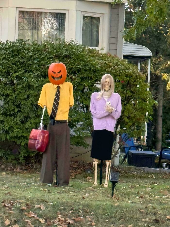 Halloween outdoor decorations featuring a pumpkin-headed figure and skeleton dressed in human clothes on a lawn.
