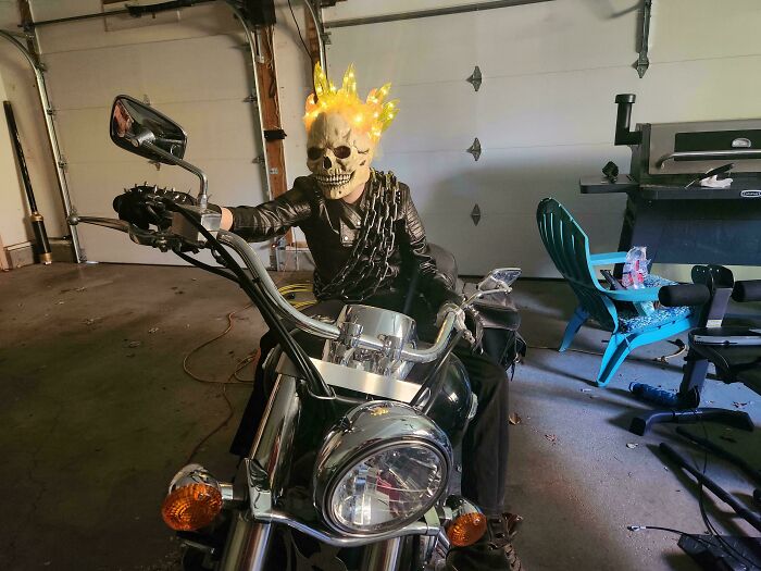 Child in amazing Halloween costume with glowing skull mask and chains sitting on a motorcycle indoors for kids' Halloween costume ideas.