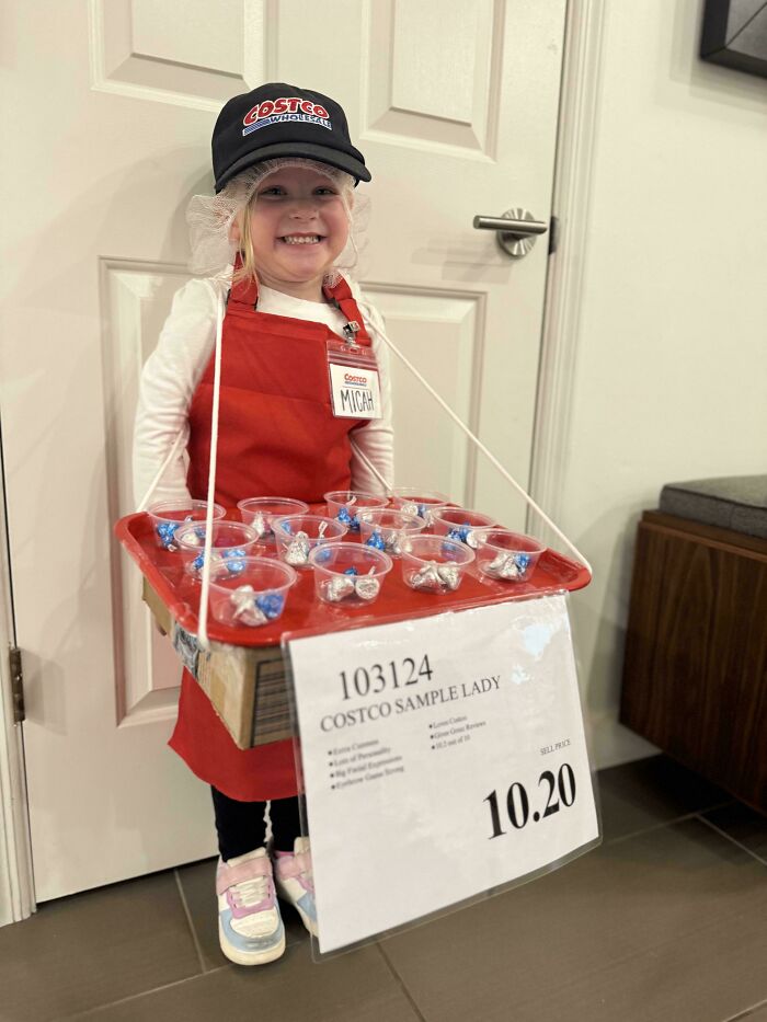 Smiling child in a creative Halloween costume dressed as a Costco sample lady with tray and name tag indoors.