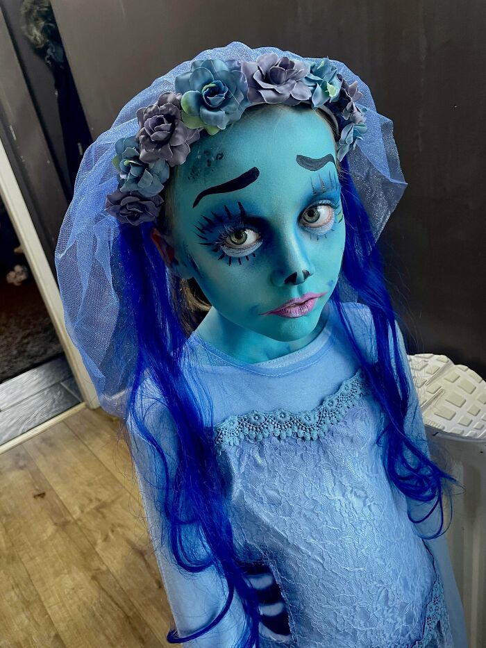 Child in an amazing kids Halloween costume with blue face paint, floral headpiece, and long blue hair for spooky fun.