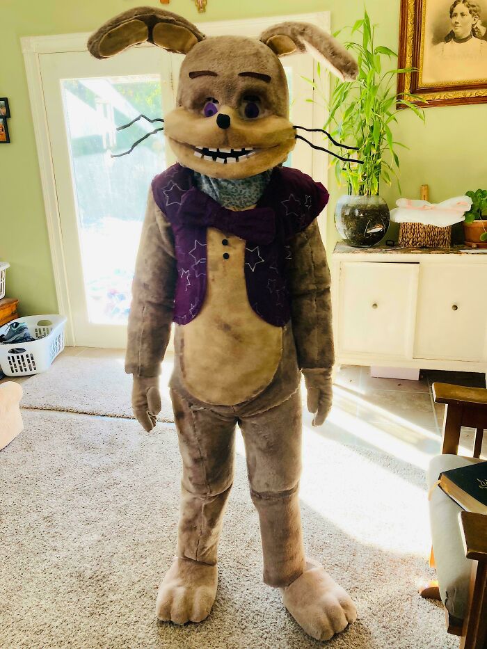 Child in an amazing kids Halloween costume dressed as a large bunny with a purple vest and bow tie indoors.