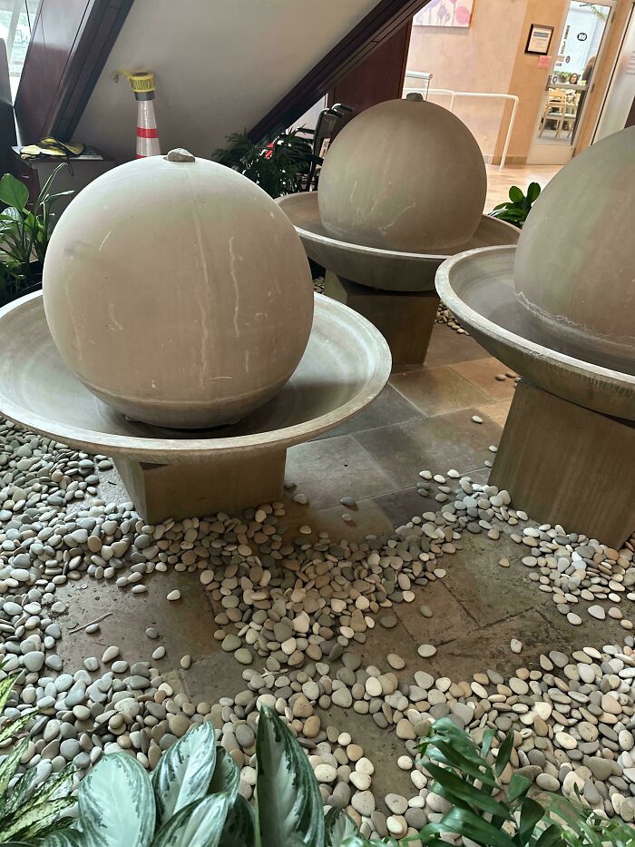 Indoor decorative stone fountains surrounded by pebbles and plants in a calming hospital waiting area setting.