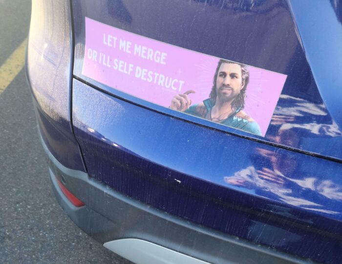 Funny bumper sticker on blue car bumper reads let me merge or I'll self destruct with character pointing, spotted by drivers on the road.