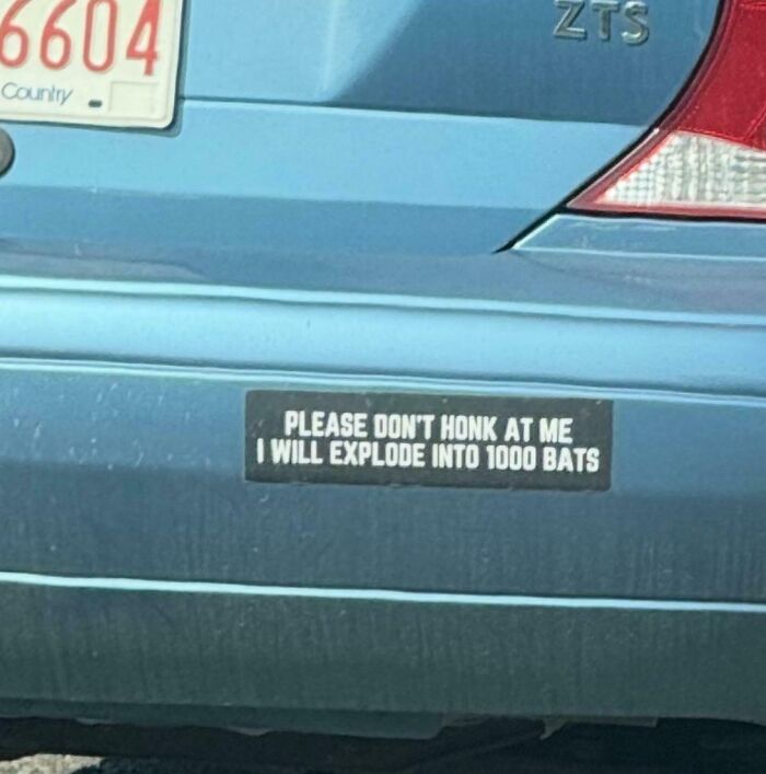 Blue car with a clever and hilarious bumper sticker warning not to honk or it will explode into 1000 bats on the road.