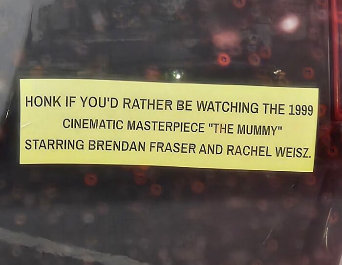 Yellow bumper sticker on a car tailgate with a clever and hilarious message about honking and watching a 1999 movie.