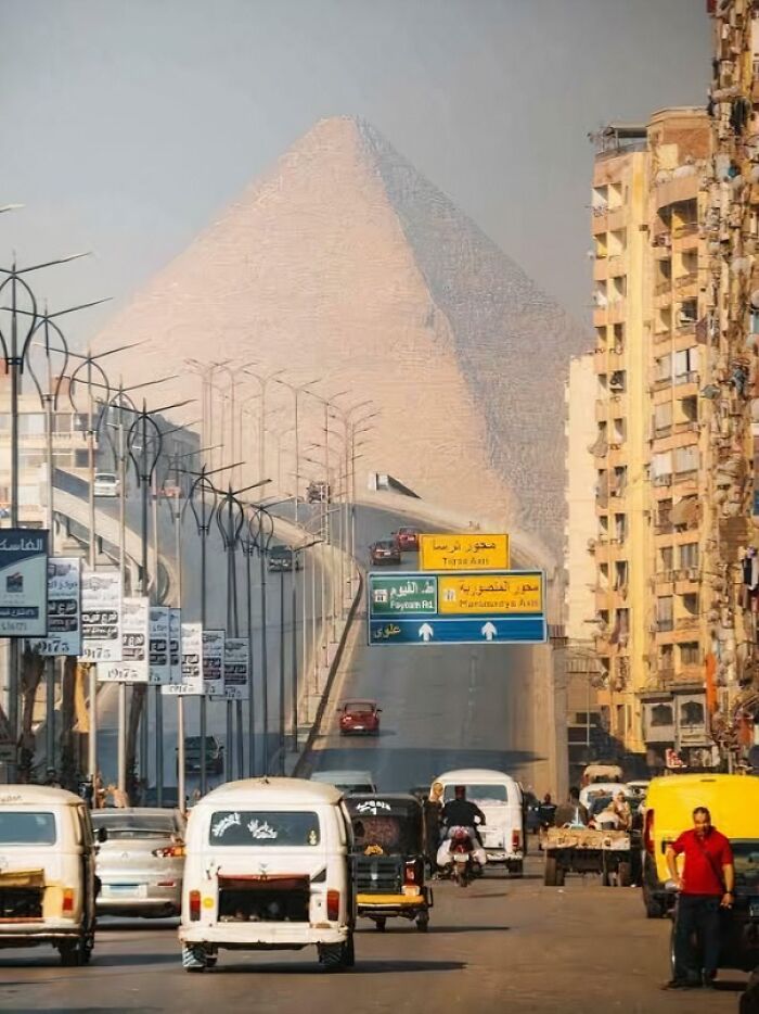 Busy street in Cairo with cars and buildings, featuring a large pyramid in the background, one of the fascinating photos.