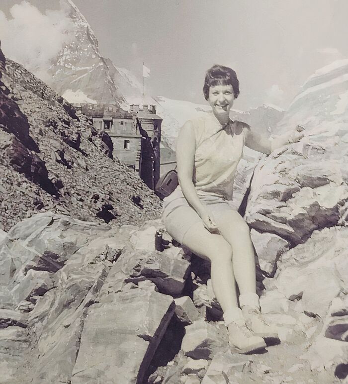 Vintage vacation pic of a woman smiling and posing on rocky mountain terrain, showing life before cell phones with cameras.