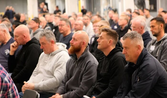 A group of men attentively listening during a community event, representing men are good in society.