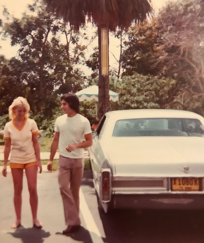 Couple walking near a classic car in a vintage vacation photo from a time when cell phones didn’t have cameras.