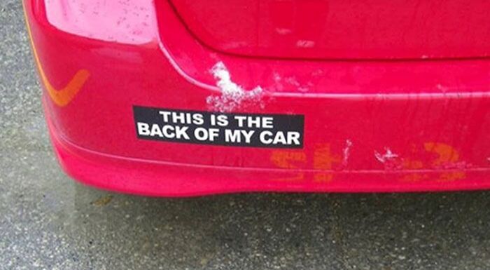 Red car with a clever and hilarious bumper sticker that reads "This is the back of my car" on the rear bumper.