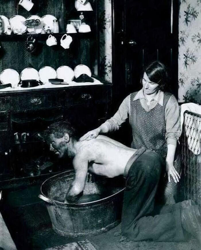 Woman helping a coal miner wash in a basin, an intriguing historical photo showing daily life and work stories.