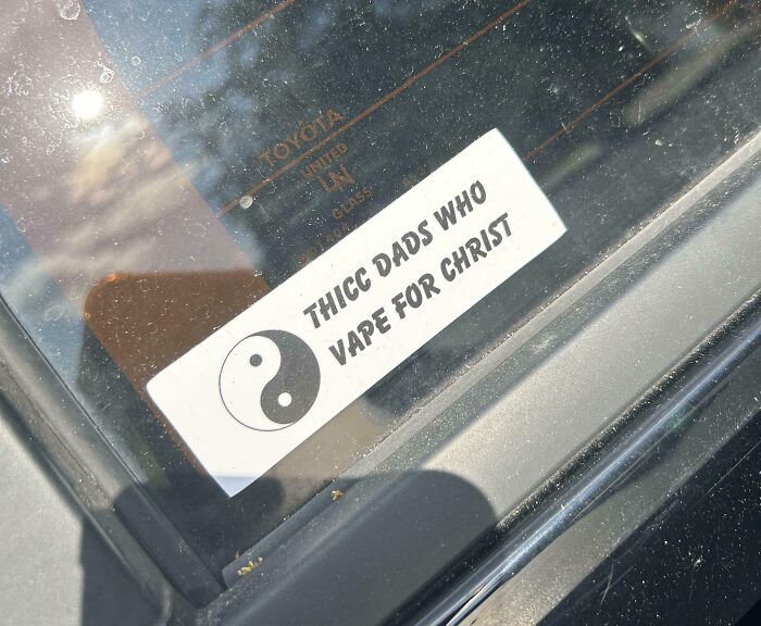 Sticker on a car window with a yin-yang symbol and the humorous text about dads vaping for Christ, clever bumper stickers on the road.