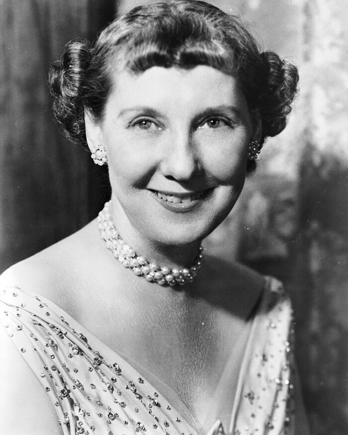 Black and white portrait of a smiling woman wearing a pearl necklace and earrings, vintage historical photograph.