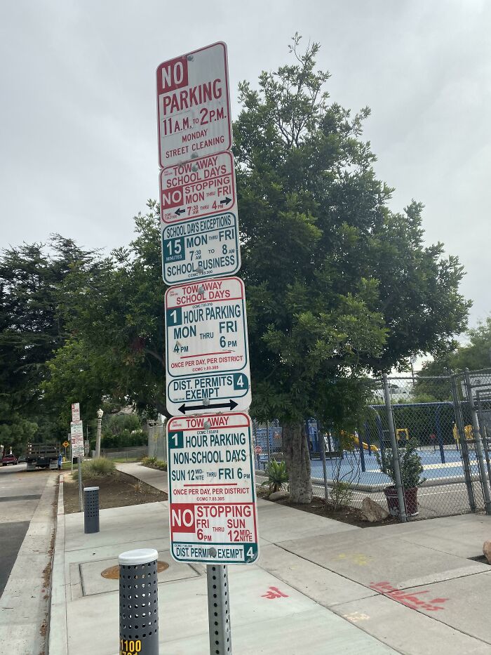 Confusing road signs with multiple parking restrictions and tow-away rules on a street corner under cloudy sky.