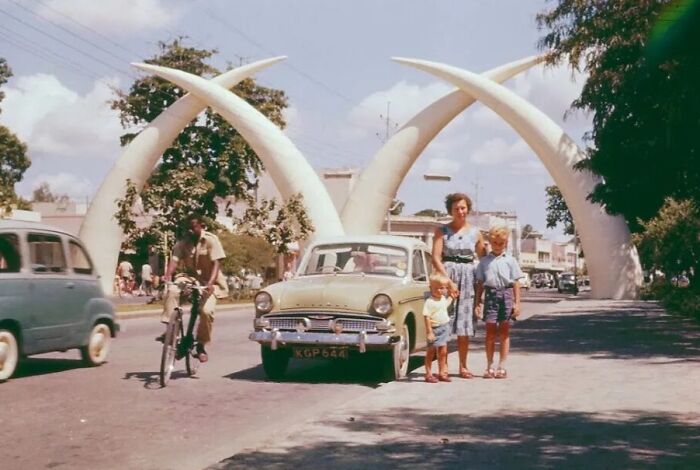Vintage vacation scene with family and classic car near landmark tusks, showcasing vacation pics from before cell phone cameras.