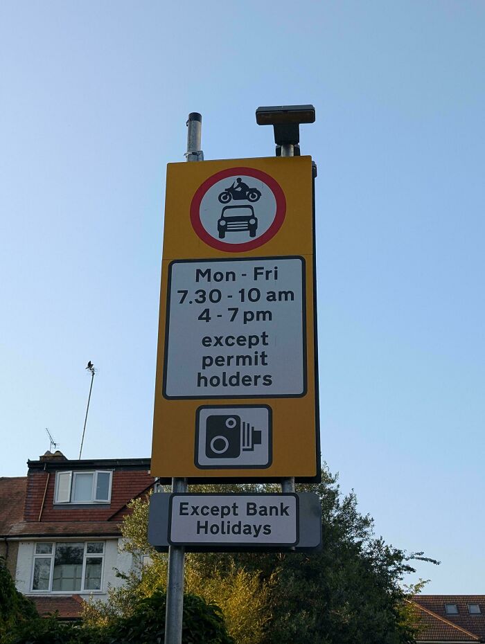 Road sign showing restricted vehicle times with permit exceptions and camera enforcement, confusing for drivers to ignore GPS.