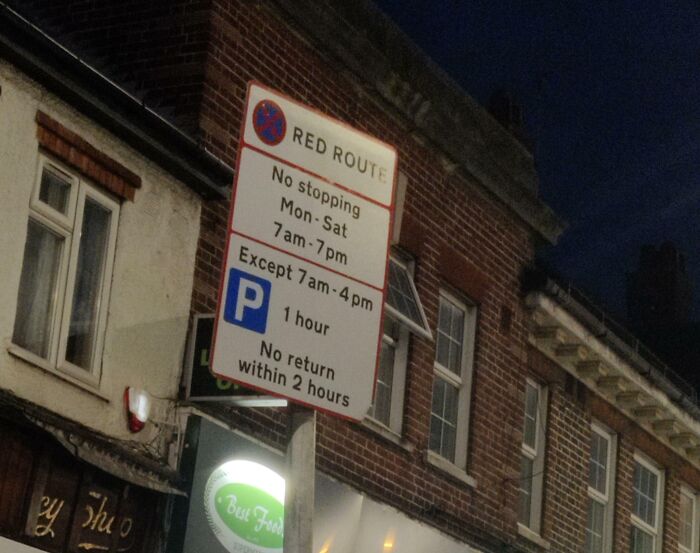 Confusing road sign showing parking restrictions and no stopping times on a red route at night.