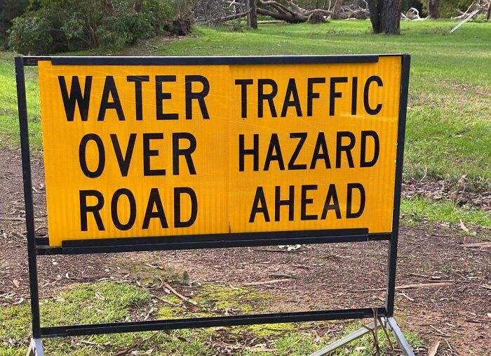 Yellow road sign warning of water over road and traffic hazard ahead, illustrating confusing road signs people ignore GPS for.