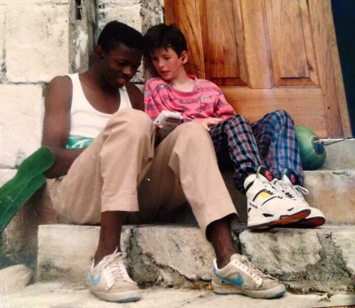 Two friends sitting on stone steps looking at a device in a nostalgic vacation pic from a time before cell phone cameras.