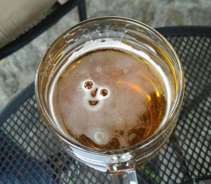 Foam in a glass of beer forming a weird face, creating a blessed and cursed moment in a strange picture.