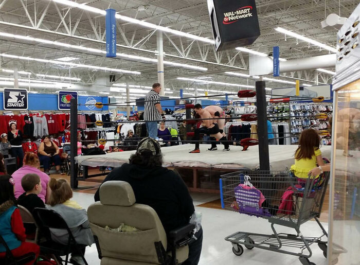 Wrestling match inside a Walmart store with audience sitting in chairs and shopping carts watching the bizarre event.