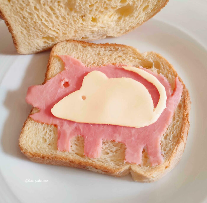 Slice of bread with ham cut as a pig and cheese shaped like a mouse, a weird and blessed food art picture.