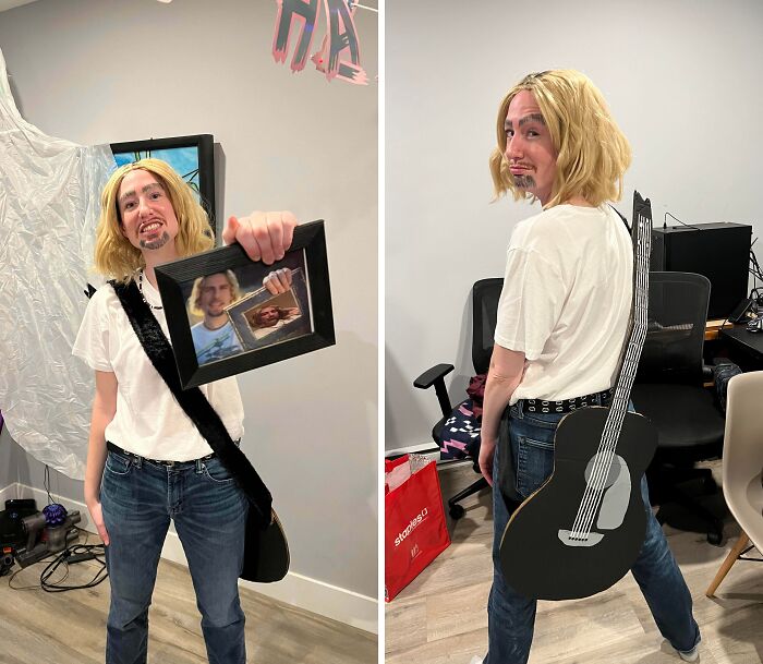 Person in a genius Halloween costume with a blonde wig, painted facial hair, and a cardboard guitar prop at a party.