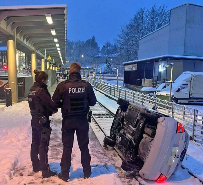 Two police officers standing near an overturned car on snowy train tracks in an unphotoshopped real scene.