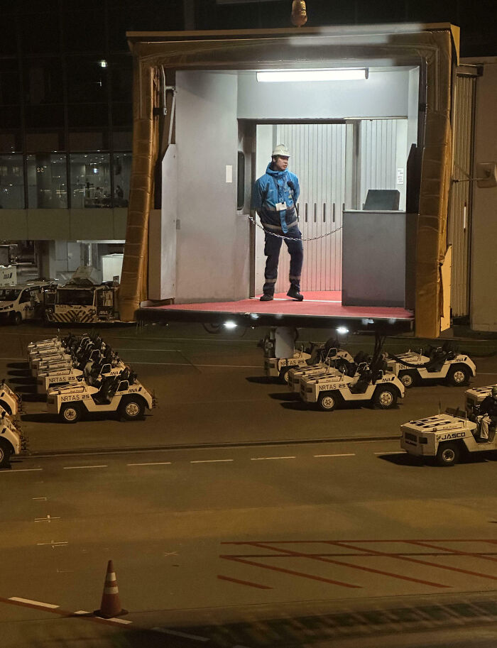 Airport worker standing still on a jet bridge platform that appears to float, an unphotoshopped pic that looks fake but is real.