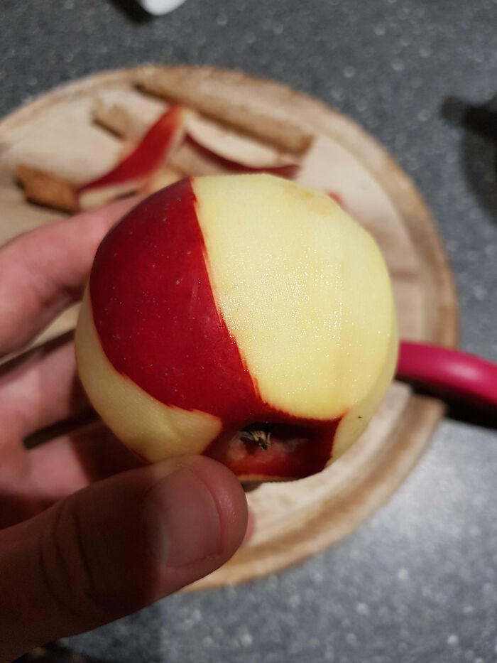 Hand holding an unphotoshopped apple partially peeled to reveal red and yellow skin in a way that looks fake but is 100% real