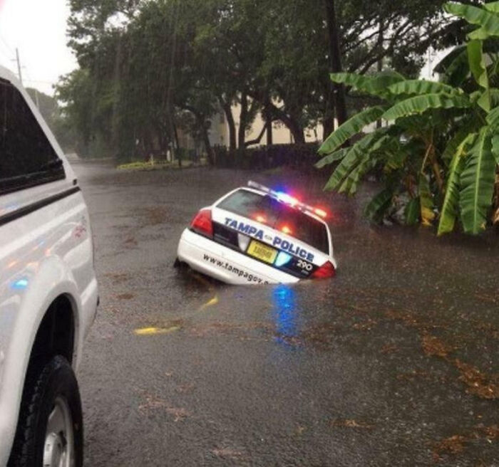 Police car partially submerged in floodwater, with emergency lights on, showcasing an unphotoshopped real scene that looks fake.
