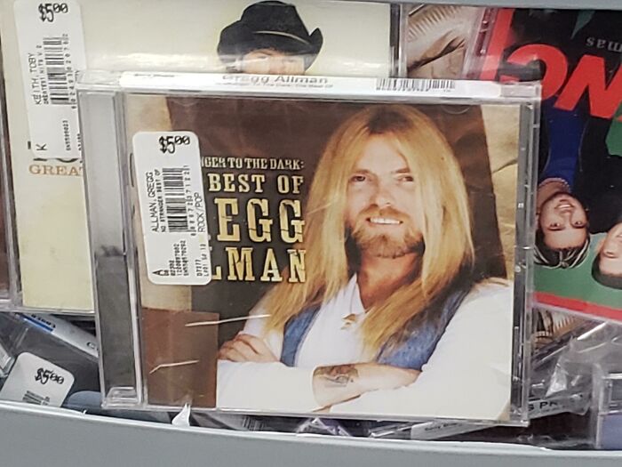 CD cover with long-haired man titled Best of Egg Alman, among other humorously displayed music cases in meme-worthy photo.