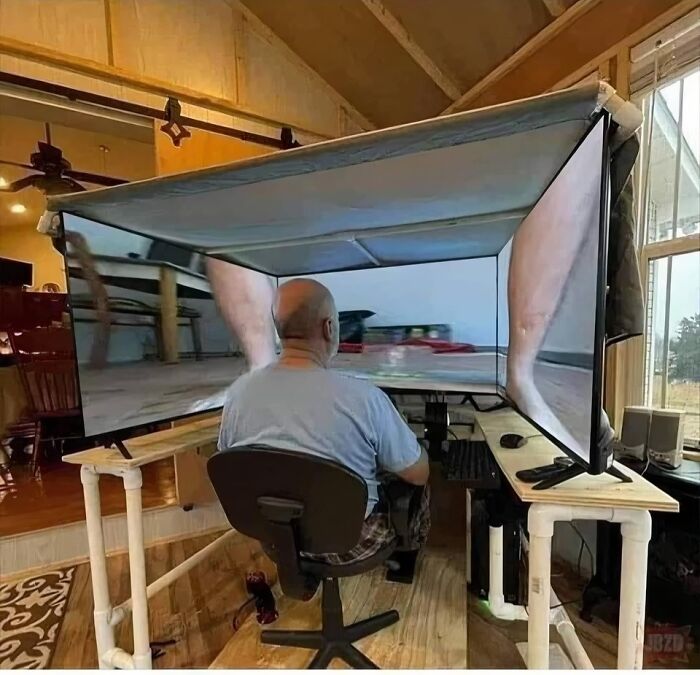 Man seated at a triple monitor setup displaying distorted images, creating an out of context and humorous occult scene indoors.