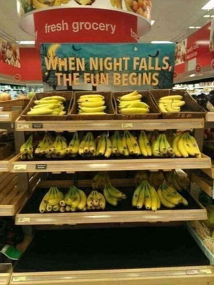Grocery store banana display with a humorous occult-themed sign saying when night falls the fun begins.