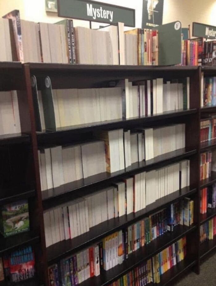 Bookshelves labeled mystery filled with blank white book covers in a bookstore, evoking pleasures of the occult humor.