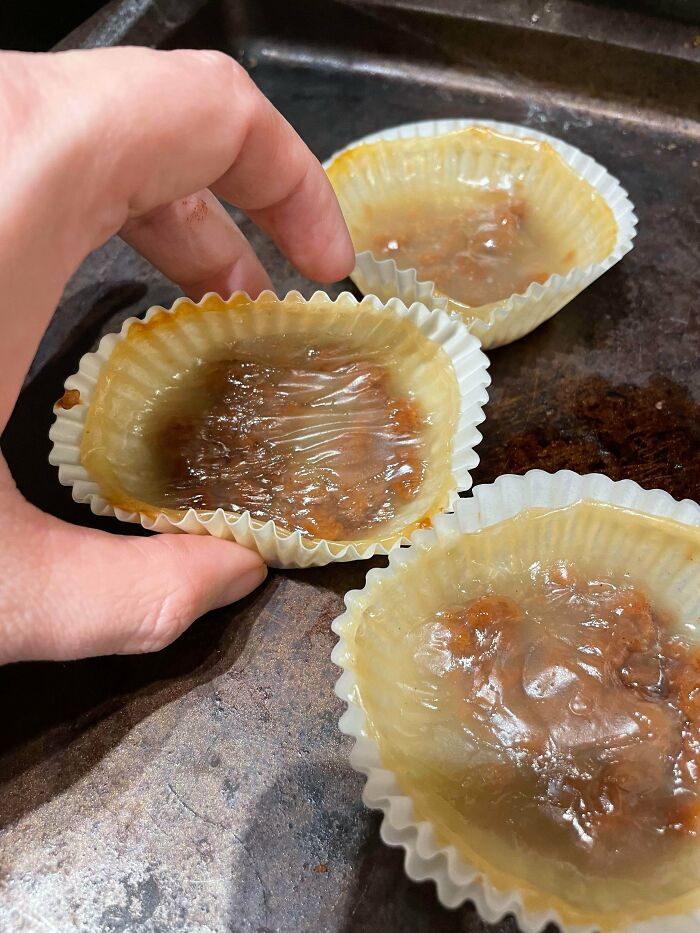 Close-up of hand holding a paper cup with a translucent, unappetizing, and gooey food substance on a baking tray.