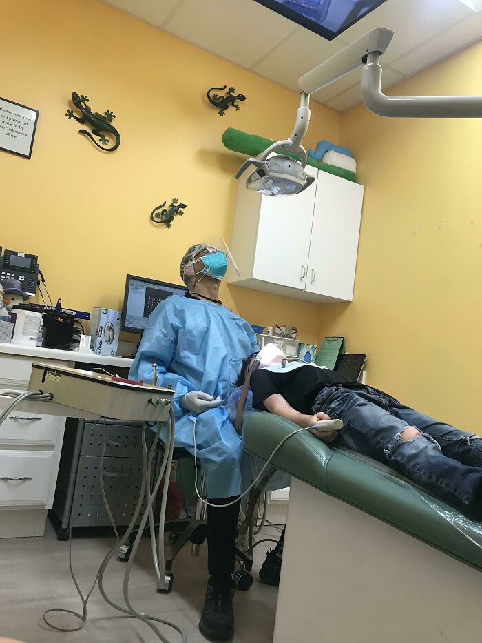 Dentist in protective gear treating a patient in a colorful room with wall decorations to ease patients.