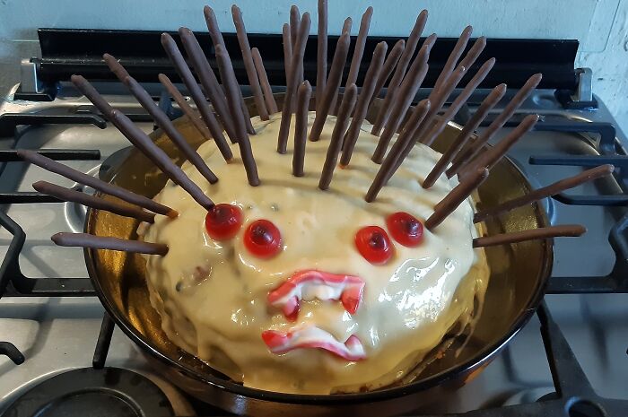 Cake with chocolate sticks and red candy decorations creating a cursed and disgusting food appearance on a stove.