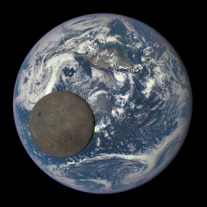 Dark side of the moon partially covering Earth with visible clouds and land in this epic astronomy photo of space.