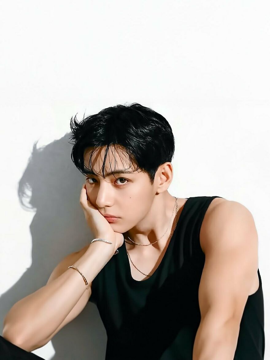 Young Kim Tae-Hyung with black hair and sleeveless black top posing thoughtfully, representing most handsome man in the world 2025.