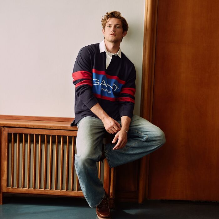 Young man in casual outfit sitting indoors, posing confidently as a contender for most handsome man in the world 2025.