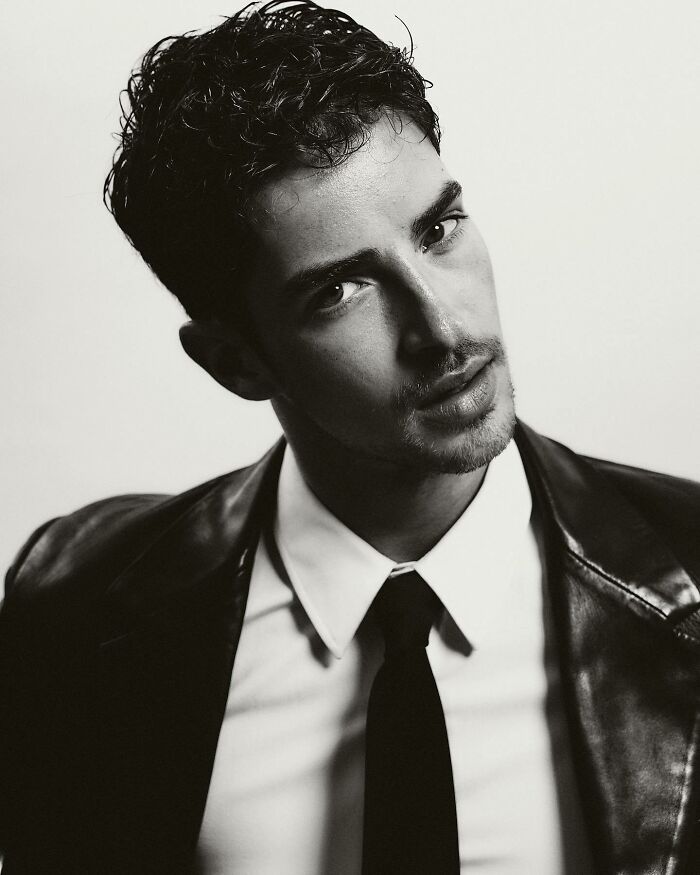Close-up black and white portrait of a stylish man with curly hair, wearing a leather jacket and tie, handsome man in the world.
