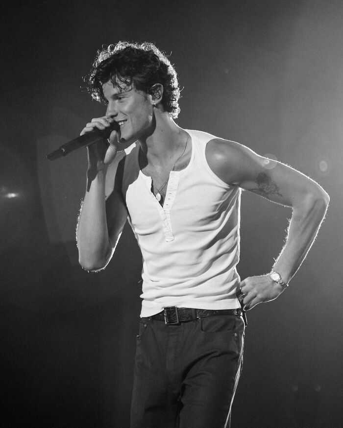 Male singer performing on stage wearing a white sleeveless shirt, representing the most handsome man in the world 2025.
