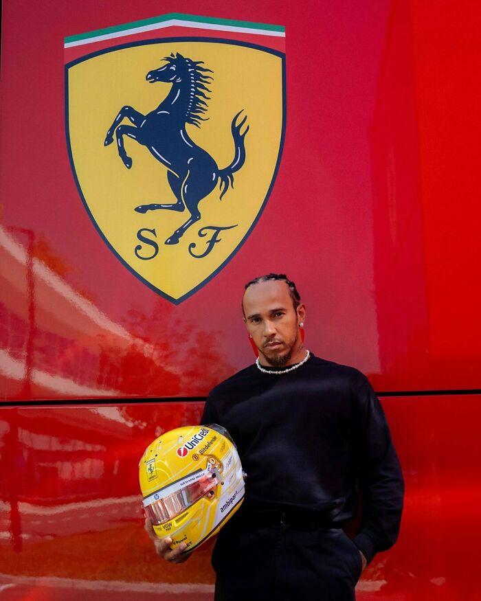 Man posing with Ferrari logo in background holding yellow racing helmet, symbolizing handsome man in the world 2025.