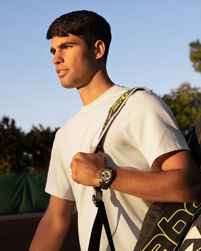 Young man posing outdoors with tennis bag, wearing a white shirt and watch, representing most handsome man in the world 2025.